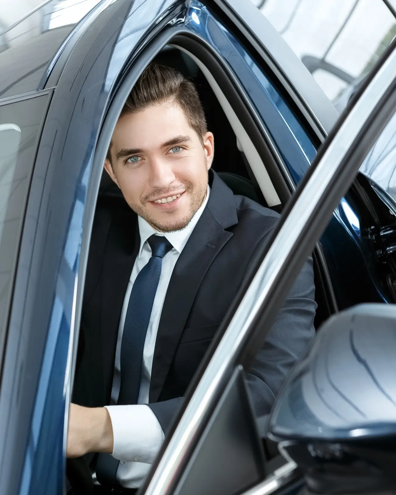 Home Smiling driver in a suit sitting in a car with the door open